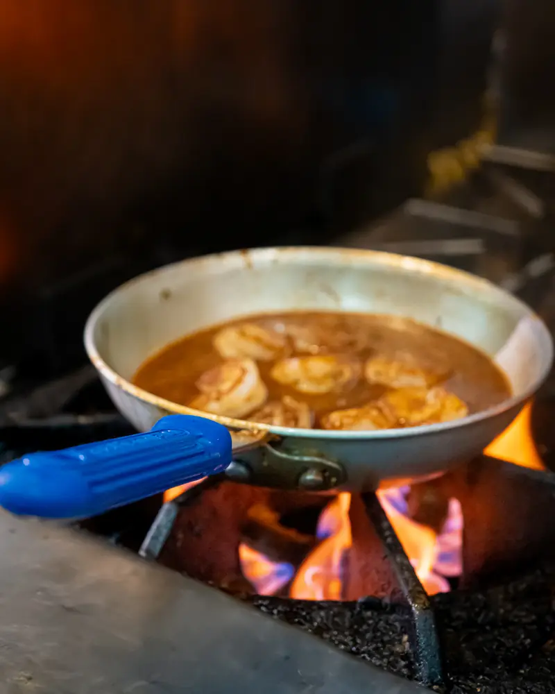 Garlic shrimp sizzling in a pan over an open flame in the Agave Social kitchen