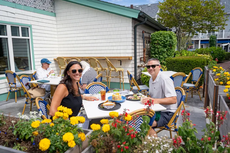 Guests at a patio table among blue bistro chairs and yellow marigolds