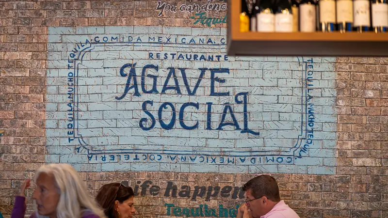 The hand-painted Agave Social badge on the brick wall of the dining room, with guests at tables below