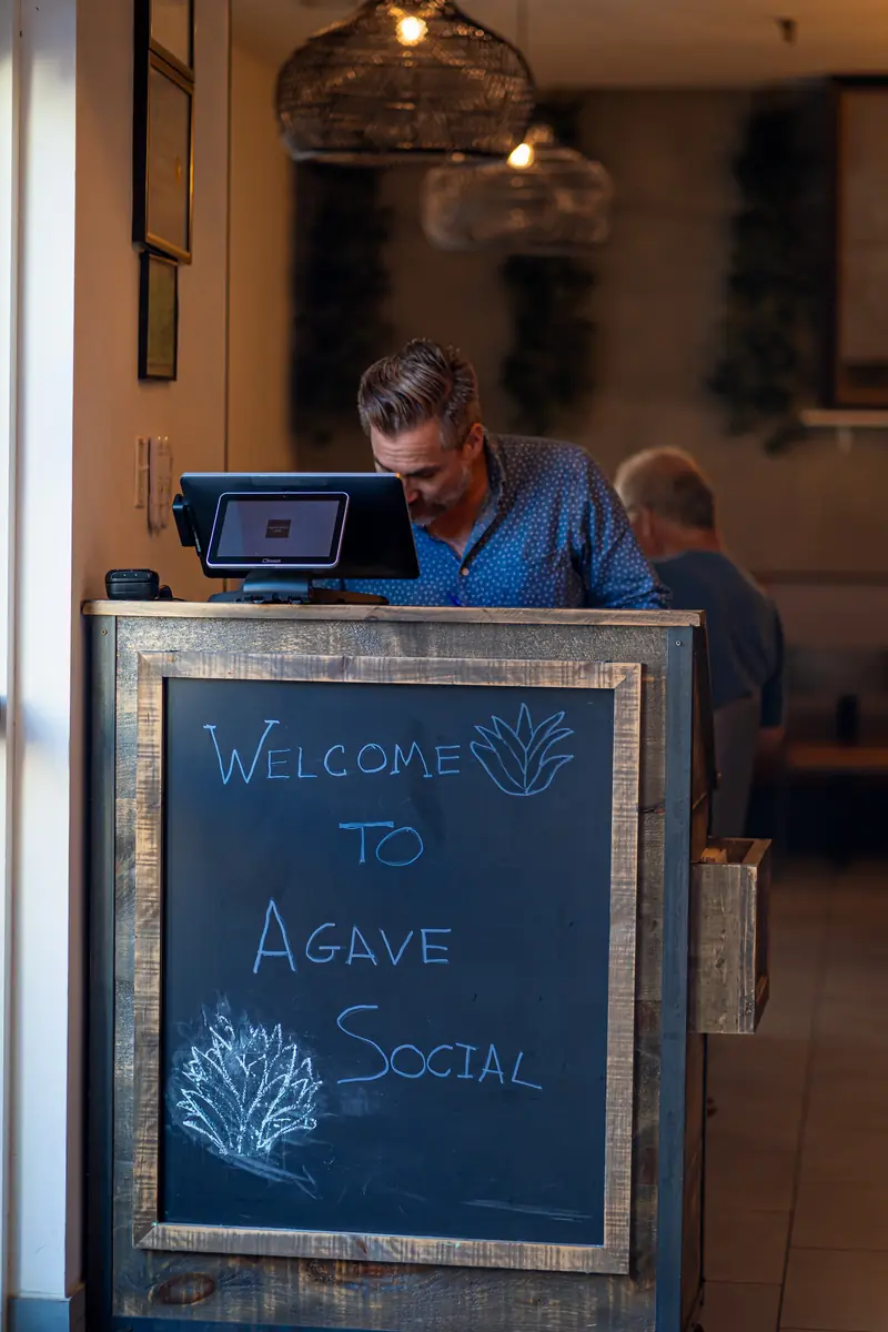 The host stand at the entrance with a Welcome to Agave Social chalkboard