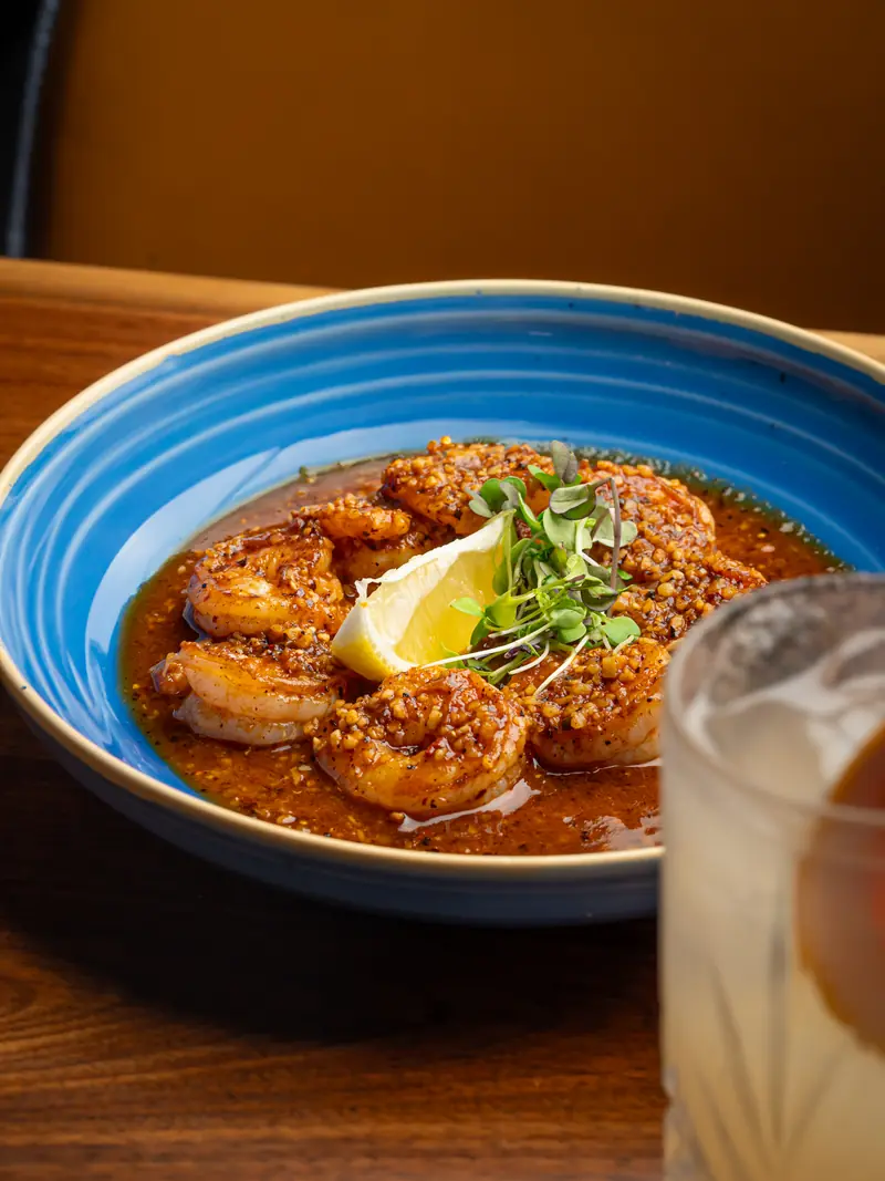 Garlic shrimp in a red roasted arbol sauce in a blue ceramic bowl with lemon