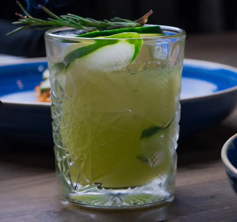 A cucumber cocktail with a rosemary sprig over ice
