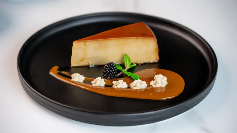 A wedge of flan with caramel sauce, a blackberry and mint