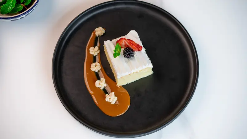 Tres leches cake with a strawberry, a blackberry and a caramel swoosh