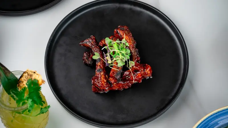 Glazed ribs with microgreens on a black plate