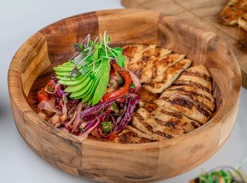 Grilled chicken with avocado, pickled cabbage and peppers in a wooden bowl