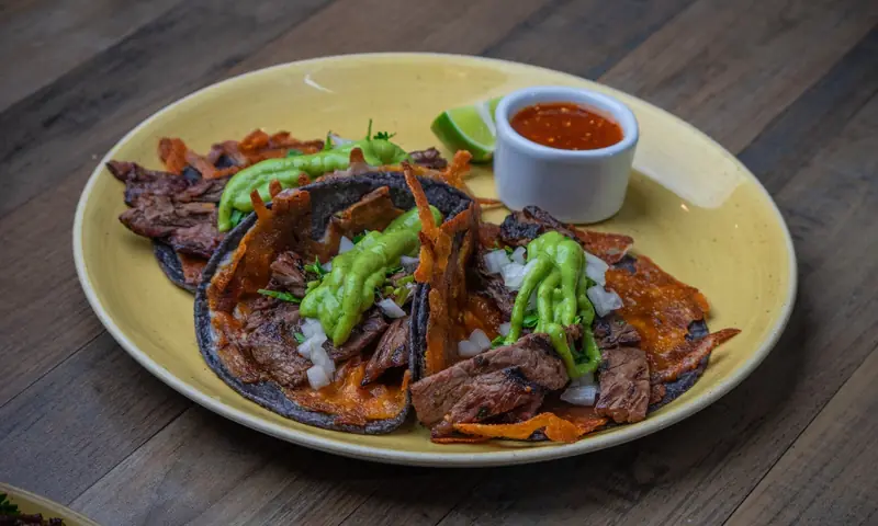 Steak tacos topped with guacamole and onions, with a side of salsa