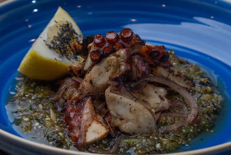 Grilled octopus with charred onion and salsa verde in a blue bowl